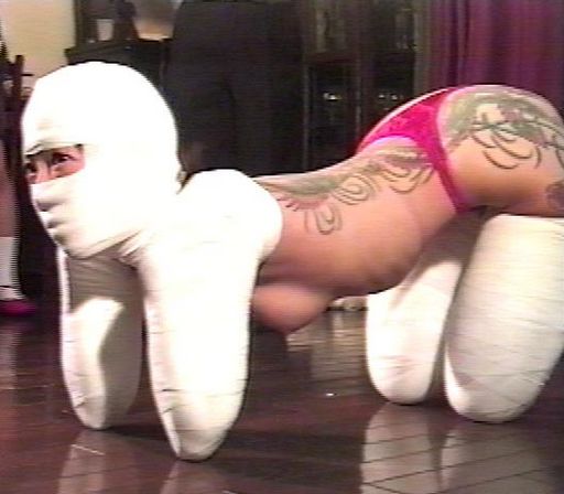 japanese woman on her knees and elbows with her hands and feet bound up in bondage tape and her face hidden in a plaster cast