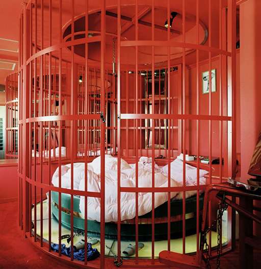 bed fully enclosed in a round red steel floor-to-ceiling barred cage