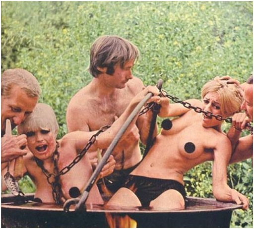 two girls poorly and loosely chained in a steaming cauldron over a fire as three men seem intent on making them into soup