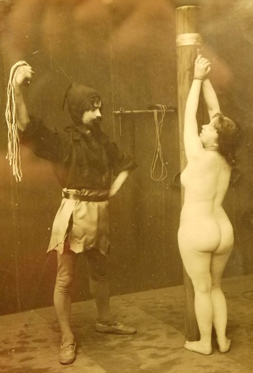 vintage erotica photo of a naked woman tied to a post for a flogging with ropes