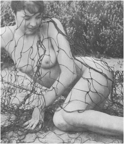 nude woman all wrapped up in an old piece of fishing net on a sandy beach