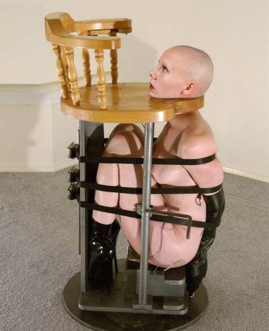 bald woman strapped into a chair for the provision of unlimited oral sex