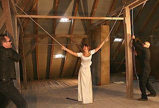 whipping girl tied with ropes to overhead beams