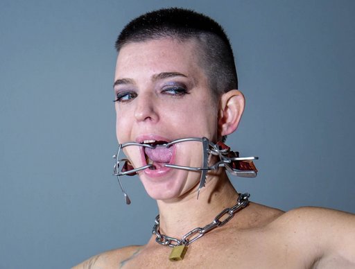 buzz cut woman wearing dental gag and padlocked chain collar