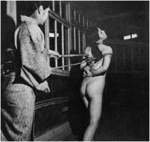naked japanese woman being controlled by a woman in a kimono through a combination of pain control techniques and rope bondage, in a prison setting