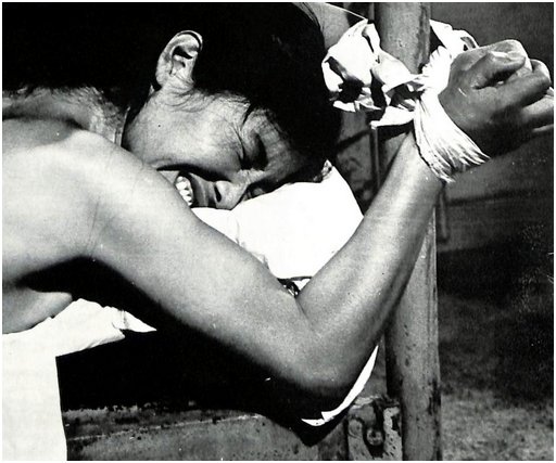 woman tied face down on an iron bed and showing an angry terrified expression